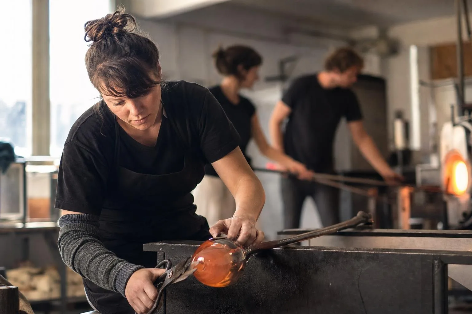 Hands turning a blowpipe of molten glass at the furnace
